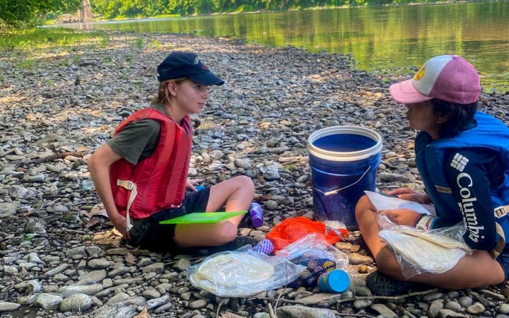 two girls sit on the shore and prepare food on an outward bound expedition